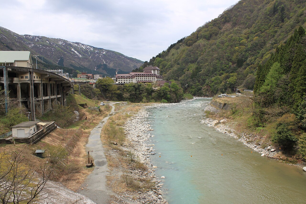 川沿いの桜並木と湯口の白い煙が重なる四月下旬の風景
